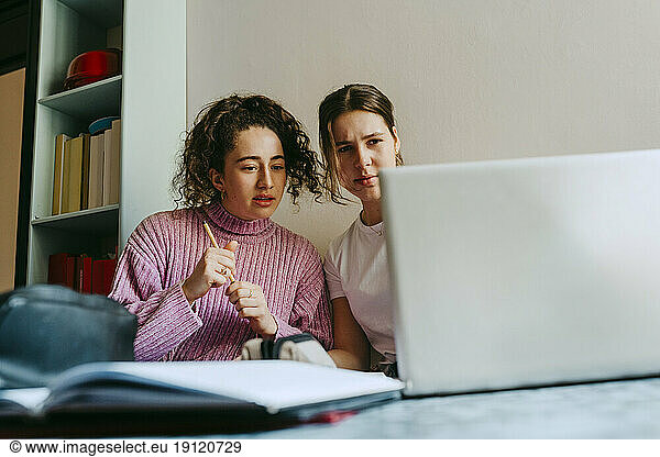 Junge Freundinnen schauen auf den Laptop  während sie gemeinsam Hausaufgaben machen