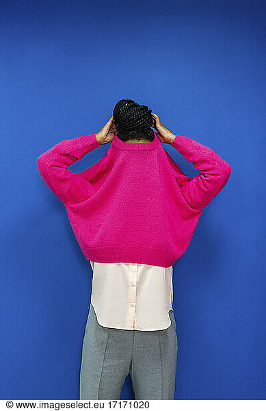 Junge Geschäftsfrau entfernt rosa Sweatshirt gegen blaue Wand im Büro