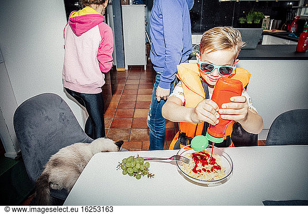 Junge gießt morgens Ketchup bei Tisch