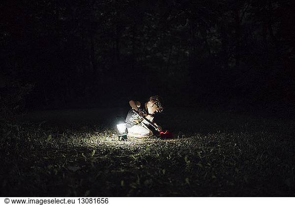 Junge gräbt mit Schaufel im Hof bei beleuchteter Laterne während der Nacht