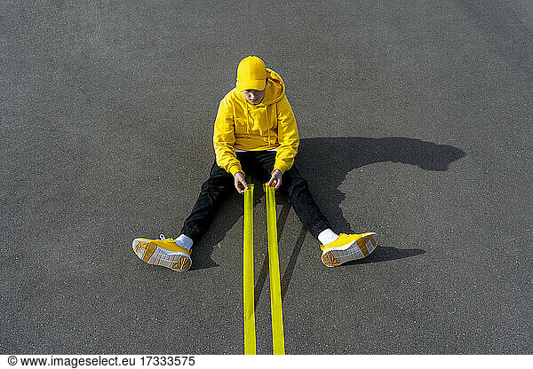 Junge hält gelbe Klebebänder  während er auf der Straße sitzt