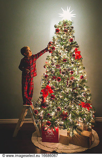 Junge hängt Weihnachtsschmuck an den Weihnachtsbaum bei Nacht