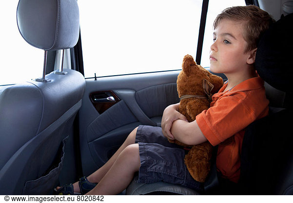 Junge im Kindersitz im Auto mit Teddybär