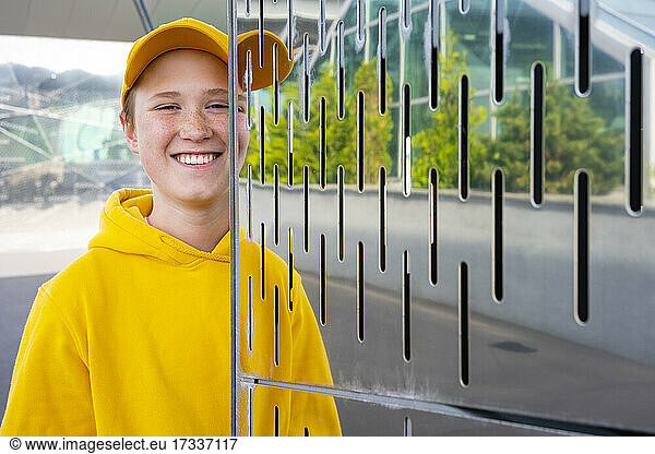 Junge in gelbem Sweatshirt lächelnd durch Metallwand