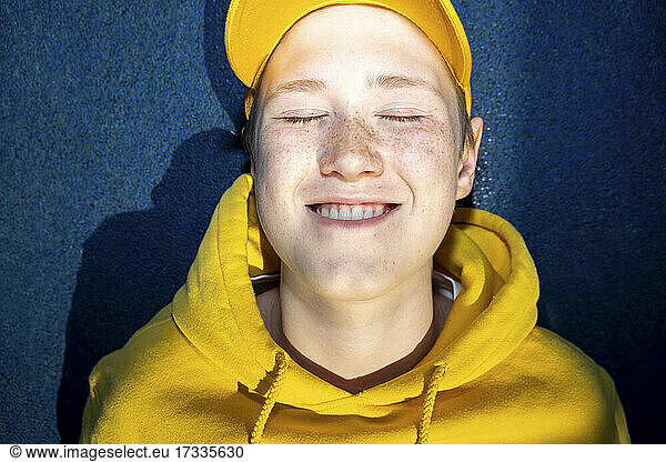 Junge in gelbem Sweatshirt lächelt mit geschlossenen Augen