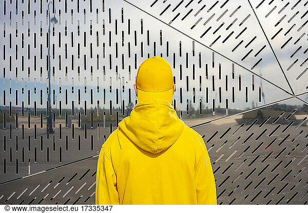 Junge in gelbem Sweatshirt vor einer Metallwand an einem sonnigen Tag