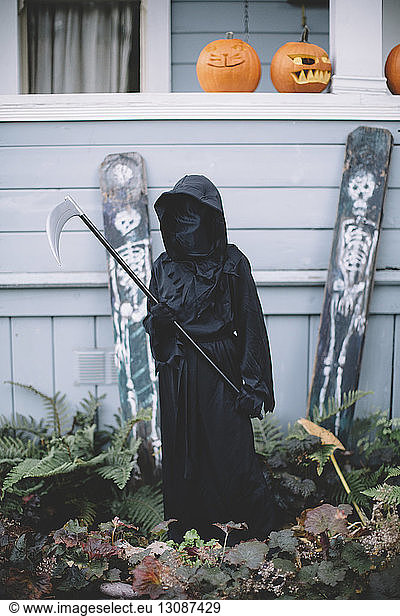 Junge in Halloween-Kostüm hält Waffe  während er im Hof beim Haus steht