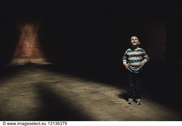 Junge in voller Länge in dunklem Raum stehend