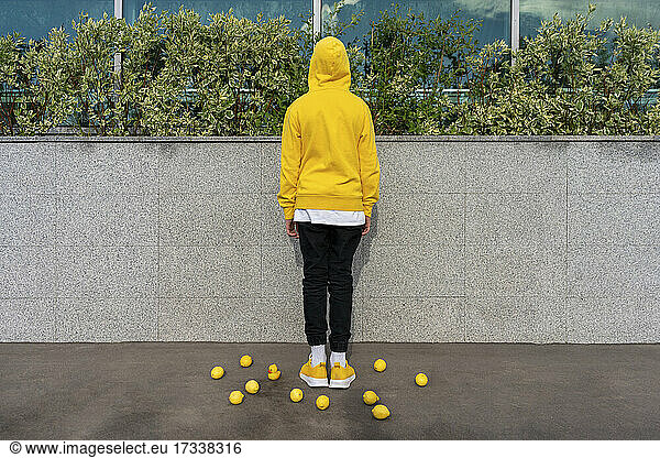 Junge inmitten von Zitronen und Gummiente vor einer Stützmauer stehend