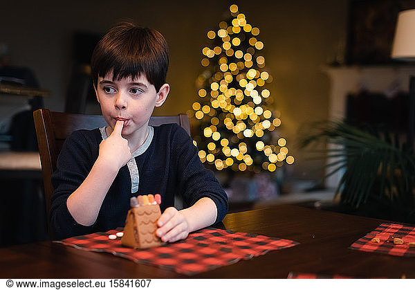Junge Junge schmückt Lebkuchenhaus mit Süßigkeiten zu Weihnachten.