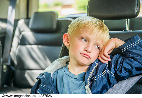 Junge Junge sitzt hinten im Fahrzeug  gelangweilter Gesichtsausdruck