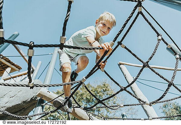 Junge klettert auf einem Spinnennetz in einem öffentlichen Park an einem sonnigen Tag