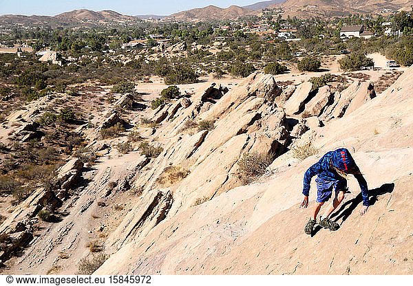 Junge klettert in der Wüste steile große Felsen hinunter