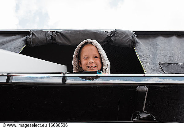 Junge lächelt vom Dachzelt beim Camping