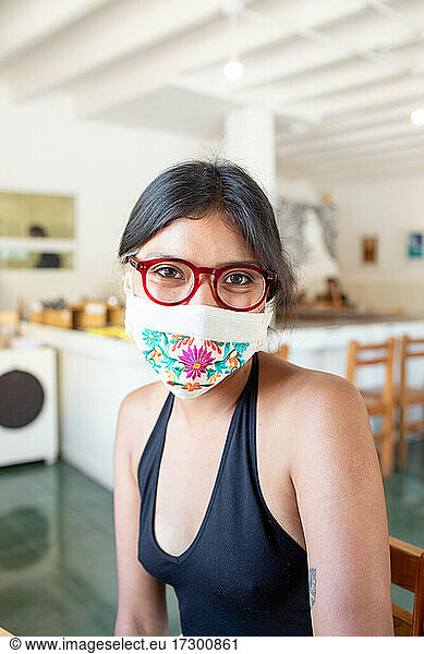 Junge lateinamerikanische Frau mit Gesichtsmaske und Brille lächelt