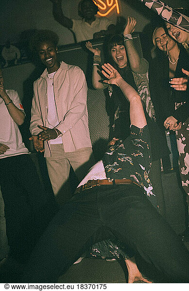 Junge Männer und Frauen bejubeln tanzende Freunde  während sie sich in einem Nachtclub nach hinten beugen