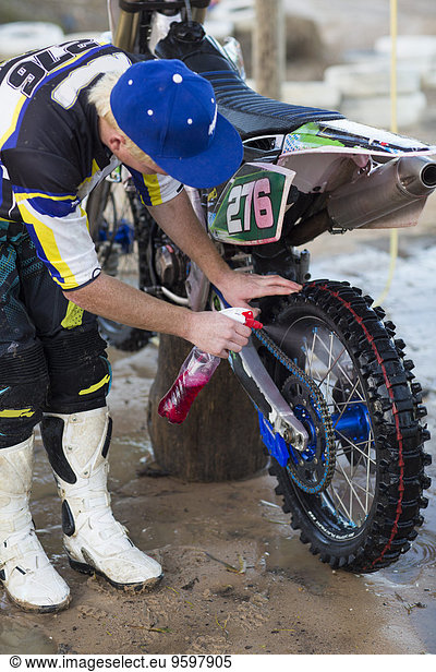 Junge männliche Motocross-Konkurrentin lehnt sich nach vorne und reinigt Motorrad
