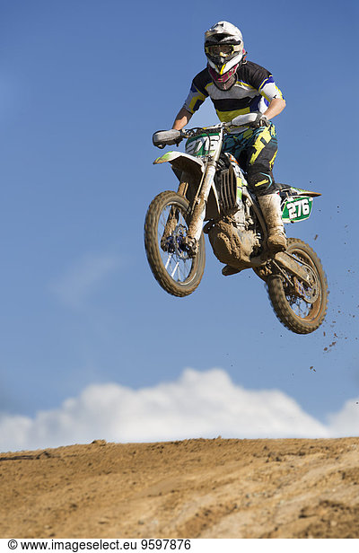 Junge männliche Motocross-Rennfahrer springen schlammig Hügel