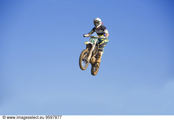 Junge männliche Motocrosser springen in der Luft gegen den blauen Himmel
