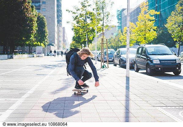 Junge männliche Skateboarder hocken beim Skateboarden auf dem Bürgersteig