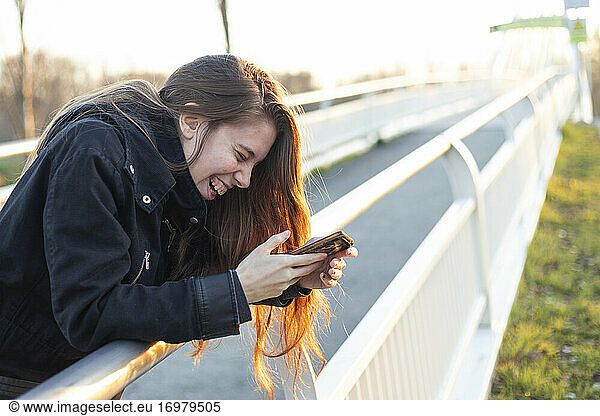 junge Millennial-Frau lacht laut und überrascht über ihr Telefon