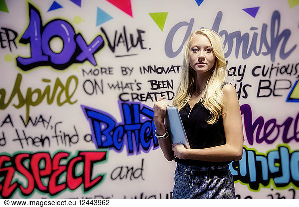 Junge Millennial-Geschäftsfrau mit ihrem Tablet vor einer bunten Wand mit motivierenden Graffiti  Sherwood Park  Alberta  Kanada