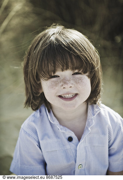 Junge mit braunen Haaren und Sommersprossen  trägt ein blaues Hemd.