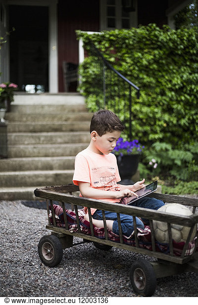 Junge mit digitalem Tablett beim Sitzen im Wagen gegen Haus