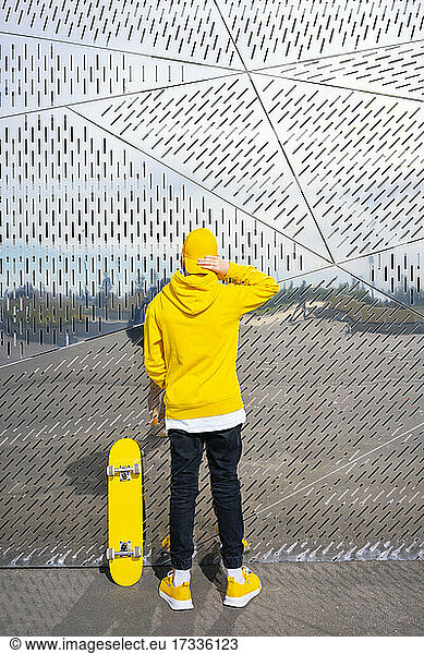 Junge mit Skateboard vor einer Metallwand
