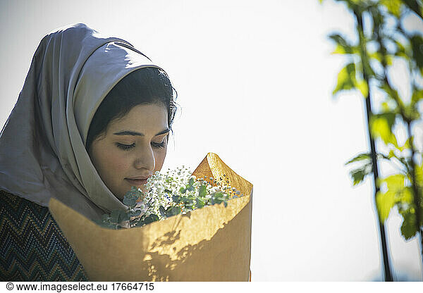 Junge muslimische Frau im Hidschab riecht an einem Blumenstrauß