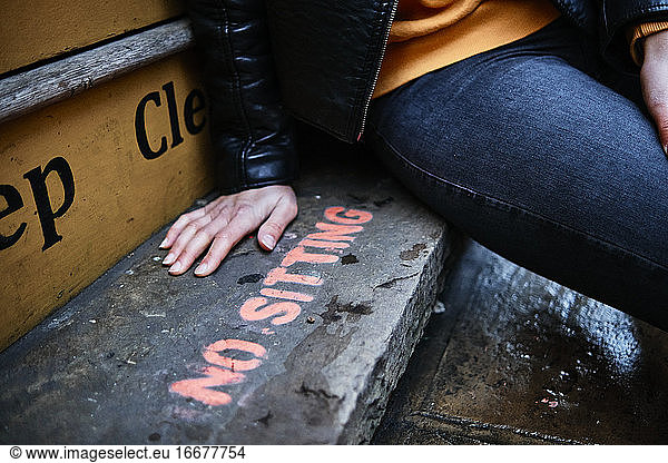 Junge  nicht erkennbare Frau  die auf einem Sitzen verboten -Schild auf dem Boden sitzt. Graffiti-Schild. Rebellisches Konzept.