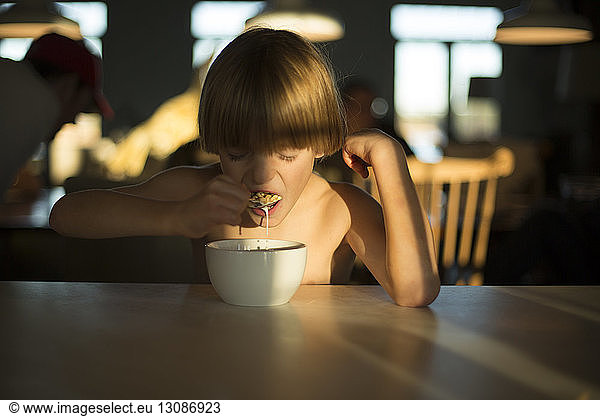 Junge ohne Hemd frühstückt am Tisch