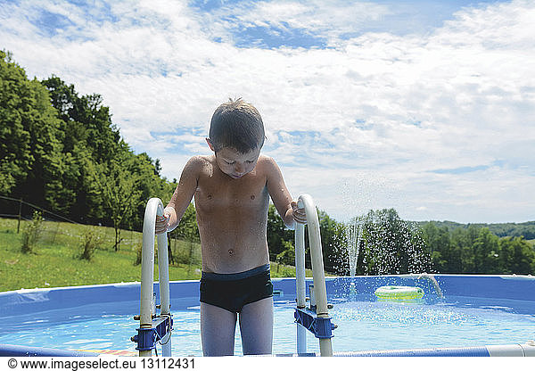 Junge ohne Hemd hält Geländer  während er im Planschbecken steht