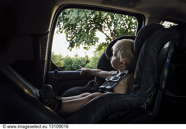 Junge ohne Hemd schaut durchs Fenster  während er im Autositz sitzt