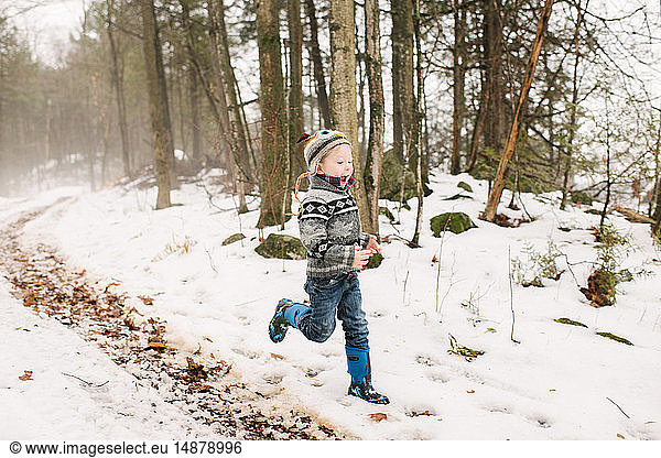 Junge rennt in Schneelandschaft durch Wald
