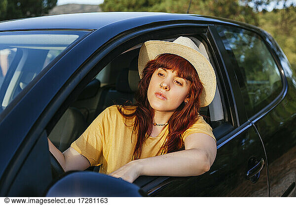 Junge rothaarige Frau lehnt sich während einer Autoreise aus dem Autofenster