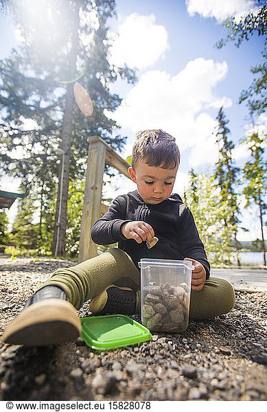 Junge sammelt Steine in einem durchsichtigen Behälter im Freien.