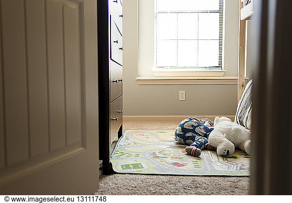 Junge schläft mit Teddybär auf Matte zu Hause