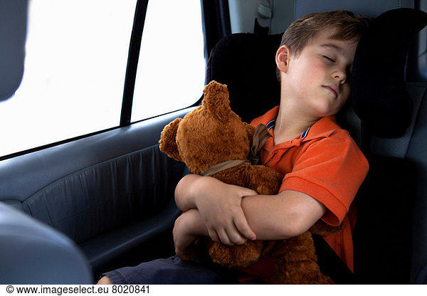 Junge schlafend im Kindersitz im Auto mit Teddybär