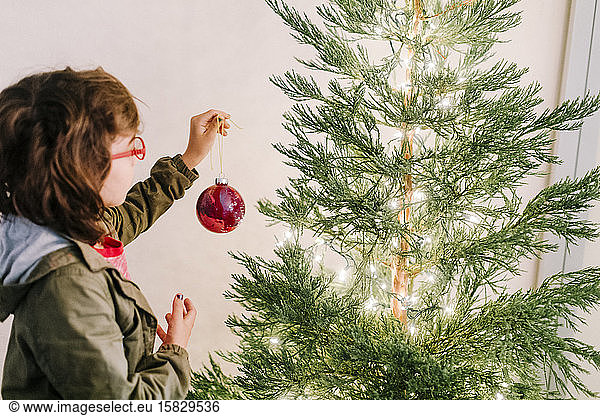 Junge schmückt Weihnachtsbaum mit erstem Ornament