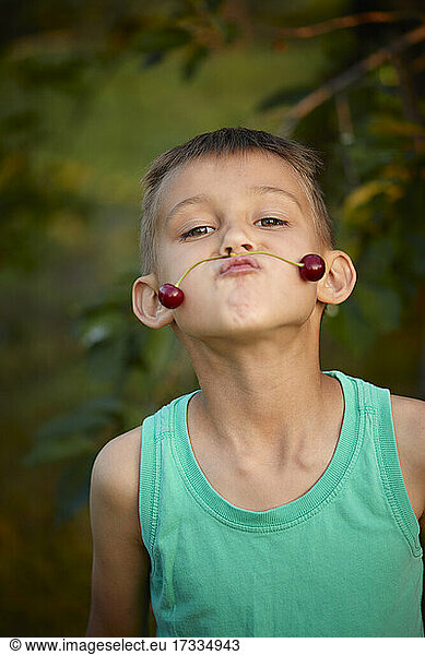 Junge schmollt  während er Kirschen als Schnurrbart auf dem Mund balanciert