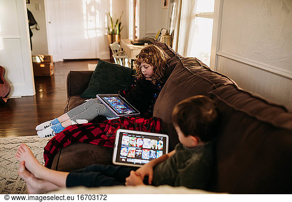 Junge Schwester und Bruder schauen Filme auf Tablets  während sie krank zu Hause sind