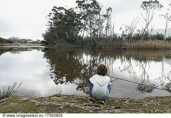 Junge sitzt am Ufer eines Flusses
