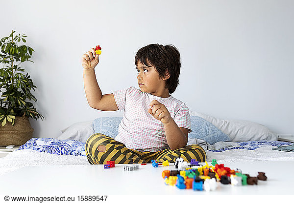 Junge sitzt auf Bett und spielt mit Bauklötzen