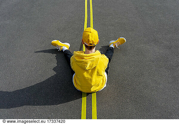 Junge sitzt über gelber Straßenmarkierung an einem sonnigen Tag
