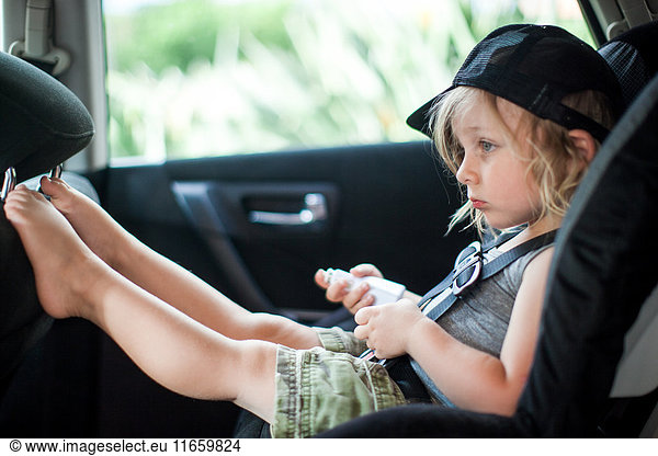 Junge sitzt im Kindersitz auf dem Rücksitz eines Autos  gelangweilter Gesichtsausdruck