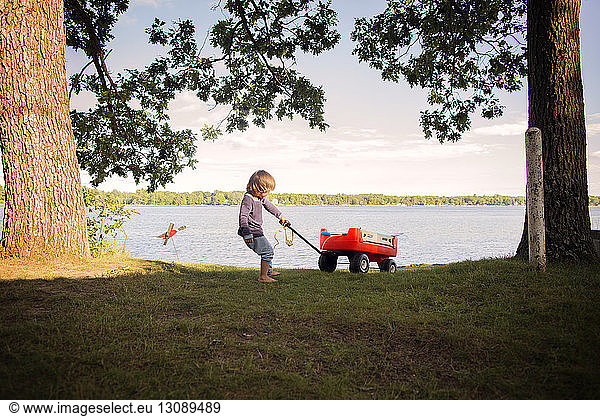 Junge spielt am See mit rotem Wagen