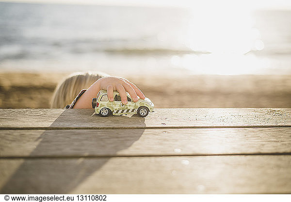 Junge spielt mit Spielzeugauto auf Holzbrettern am Strand