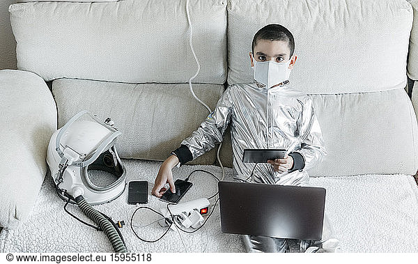 Junge spielt Spiel mit Laptop und Smartphone  trägt Raumanzug und Schutzmaske