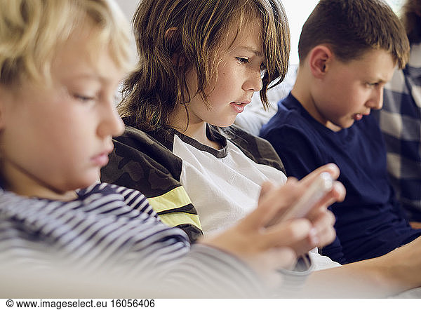 Junge spielt Spiele auf Smartphone mit Familie im Hintergrund im Wohnzimmer